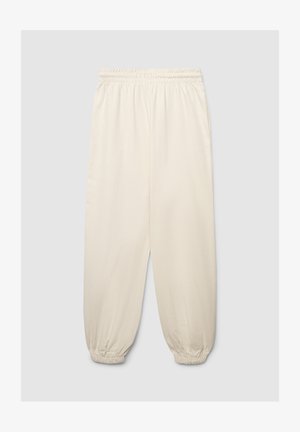 Pantaloni della tuta color beige chiaro con vita elastica, polsini arricciati e tasche ai lati, realizzati in un tessuto morbido e liscio.