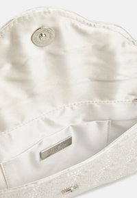 Krémově zbarvený saténový interiér kabelky se magnetickým uzávěrem, který obsahuje kovovou značkovou visačku a hladký povrch.