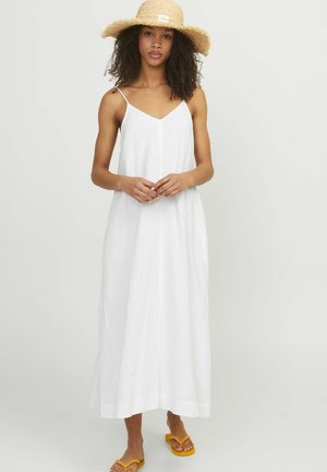 Vestido maxi blanco sin mangas con escote en V y patrón texturizado vertical. Combinado con un sombrero de paja de ala ancha y sandalias amarillas.
