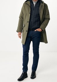 Olivgrön parkas med avtagbar svart vadderad inre jacka och mörkblå jeans. Svarta läderstövlar med snörning.