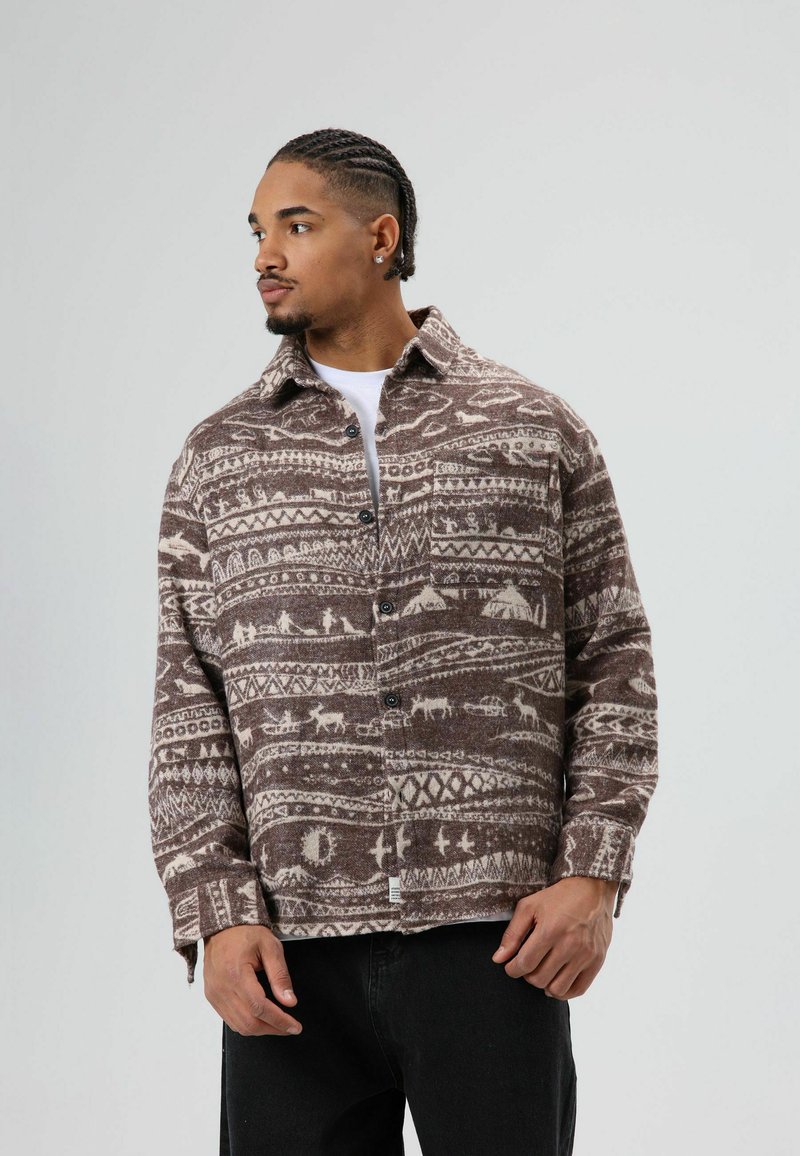 Bruin geruit flanellen overhemd met witte dierenmotieven, een knoopsluiting aan de voorkant en lange mouwen. Het materiaal is zacht met een gestructureerde afwerking.