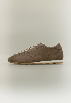 Brun ruskindssneaker med mønstret syninger, beige og hvid sål og hvide og brune stribede snørebånd vist fra siden.