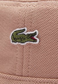 Sombrero de cubo de malla rosa con un logo de cocodrilo bordado en verde y acentos rojos. La tela texturizada proporciona una superficie transpirable.