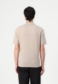 Polo à manches courtes beige en tissu lisse, avec un col classique et une coupe décontractée, associé à un pantalon noir.