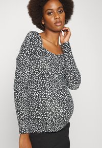 Top preto de manga longa com padrão salpicado em branco, decote arredondado e design ajustado, destacando uma silhueta arredondada.