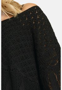 Mustat neulepusero, jossa on avonaiset olkapäät, tekstuuri virkattu kuvio ja väljä, valuva istuvuus monimutkaisella ompelutarkkuudella.