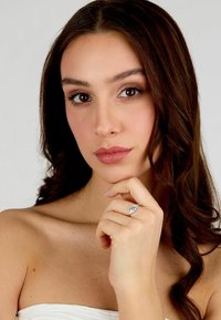 Anello di fidanzamento in argento con una grande pietra centrale, montato su una fascia liscia. Il modello posa con la mano sul mento, mettendo in mostra l'anello.