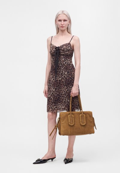 Femme aux longs cheveux blonds portant une robe à imprimé léopard et des escarpins noirs pointus à talons bas, tenant un grand sac à main en daim marron.
