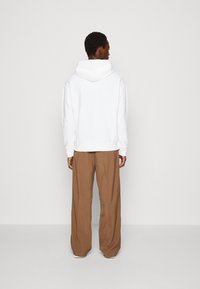 Felpa bianca con cappuccio, dal taglio rilassato, dotata di una tasca a marsupio e polsini a costine, abbinata a pantaloni marroni larghi.