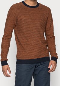 Randig orange och marinblå tröja med rund hals. Stickad struktur och ribbade ärmslut. Buren över mörk marinblå byxor.