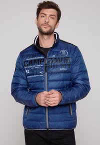 Giacca imbottita blu con zip frontale, accenti neri e numerosi dettagli stampati, tra cui coordinate geografiche e nome del marchio, design slim-fit.