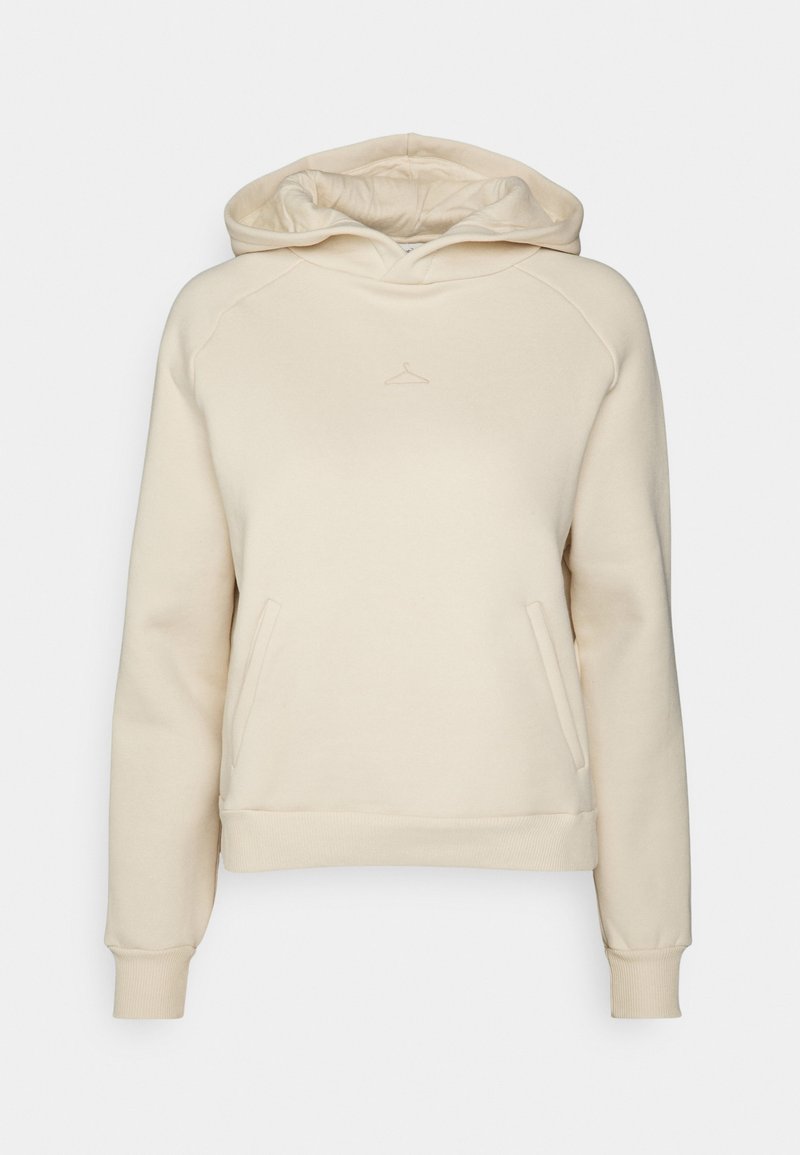 Sudadera con capucha color crema hecha de tela suave, con bolsillo tipo canguro, puños acanalados y un logo de percha bordado en el pecho.