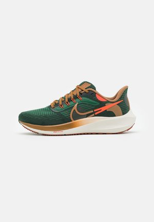 Zapatilla de correr verde y marrón con detalles naranjas, cordones beige y suela acolchada blanca diseñada para uso atlético.