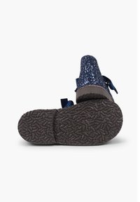 Zapato de glitera azul marino con detalle de lazo, mostrando la suela de goma texturizada. Parte superior brillante con forro interior suave, diseño de punta redondeada.