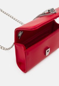 Borsa a tracolla in pelle sintetica rossa con una tracolla in catena argentata. Presenta una chiusura magnetica, scomparti interni e una superficie liscia.