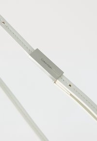 Biały skórzany pasek do zegarka z metalowym klamrą w kolorze srebrnym z grawerowanym logo. Gładka tekstura z starannym przeszyciem i regulowanymi otworami.