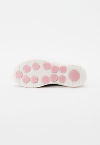 Sola do sapato com uma superfície branca texturada e grips circulares em rosa dispostos em padrões variados para tração.