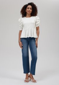 White puff sleeve top with a peplum hem, paired with blue wide-leg jeans. Model wears white strappy sandals, showcasing a casual outfit.
