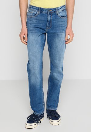 Blauwe denim jeans met een rechte pijp, voorzien van gestikte zakken, een rits- en knoopsluiting en subtiele vervaging. G gedragen met marineblauwe sneakers.
