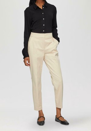 Camicia nera a maniche lunghe con colletto; abbinata a pantaloni crema a vita alta; ballerine nere con una fasciatura sopra il piede.
