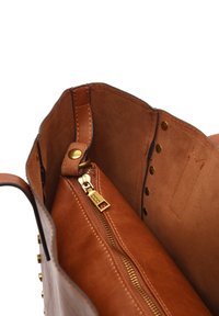 Interno della borsa in pelle marrone chiaro con una texture liscia, dotato di una tasca con zip e dettagli in metallo dorato. Chiusura a scatto visibile e rivetti.