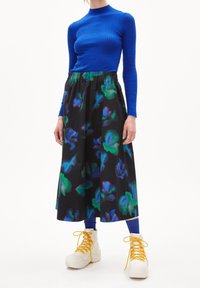 Un haut bleu à manches longues côtelé associé à une jupe noire à imprimé floral présentant des motifs verts et bleus, avec des baskets montantes blanches à lacets jaunes.