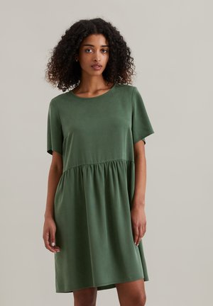Grünes kurzärmliges Kleid mit Rundhalsausschnitt und geraffter Taille. Weicher Stoff mit glatter Textur, knielanger Saum. Schlichtes Design.