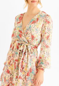 Floral wrap dress in soft, lightweight fabric. Features a v-neck, puff sleeves, and a tied waist with red, green, and yellow floral patterns.