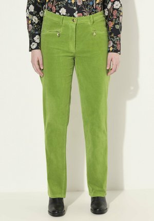 Pantalones de pana verde con un diseño de pierna recta, que cuentan con bolsillos con cremallera y un cierre de botón. Combinados con una blusa de flores de manga larga y botas negras.