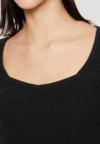 Svart stickad topp med fyrkantig halsringning, ribbad textur och sned sömdetaljer på bodice.