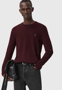 Maglione bordeaux a maniche lunghe con scollatura tonda, caratterizzato da un discreto dettaglio del logo. Abbinato a jeans scuri e una borsa nera dalla texture particolare.