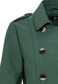 Zielony płaszcz typu trencz z kołnierzem z wycięciami, dwurzędowym zapięciem i srebrnymi guzikami. Gładka faktura z minimalną ilością detali.