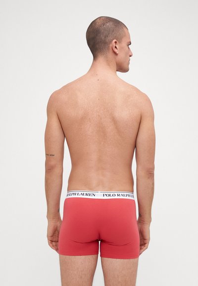 Boxeri roșii din țesătură elastică, cu un elastic alb pe care este inscripționat "POLO RALPH LAUREN" cu litere negre. Textură netedă, design ajustat.