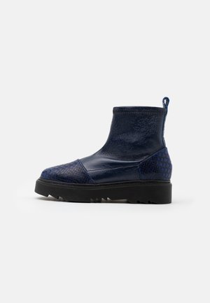 Bottine bleu marine à la cheville avec bout et talon texturés, dessus lisse, semelle noire épaisse et rainurée, et languette au talon.