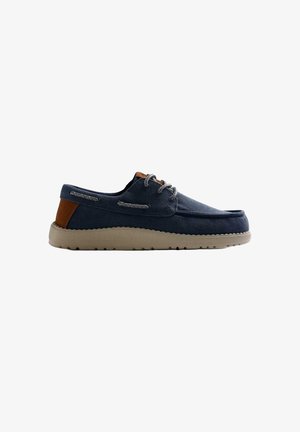 Scarpa casual blu navy con lacci, suola beige e toppa marrone sul tallone, con dettaglio laterale con lacci e tomaia in tessuto testurizzato.