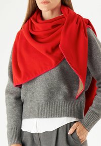 Rode wollen sjaal over een grijze gebreide trui, met een geribde zoom en contrasterende roze stiksel langs de randen. Witte shirt zichtbaar eronder.