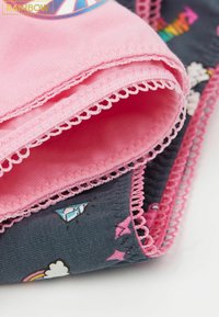 Růžová látka s vroubkovanými okraji, vrstvená nad tmavou látkou s barevnými vzory, včetně mraků a geometrických tvarů.