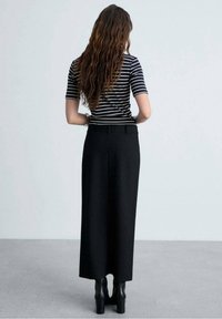 Pruhovaný top s krátkým rukávem a černá dlouhá plisovaná sukně. Oblečení má vysoký pas a hladkou texturu, doplněné černými kotníčkovými botami.