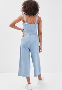 Light blue denim jumpsuit with wide cropped legs, fitted bodice, adjustable straps, and belted waist. Smooth texture with minimalist design.