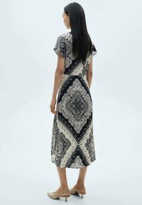 Maksi haljina od uzorkaste crno-bež tkanine, s okruglim izrezom, kap sleeves i lepršavom suknjom s elegantnim dizajnom.