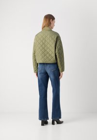 Jachetă matlasată de culoare verde măslin, cu un design scurt, având un guler în picioare și modele de tip diamant. Asortată cu blugi blue high-waisted și tocuri negre.