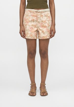 Persona che indossa pantaloncini beige con stampa floreale e cintura intrecciata, top verde oliva senza maniche e sandali con cinturini marroni, in piedi su sfondo bianco.