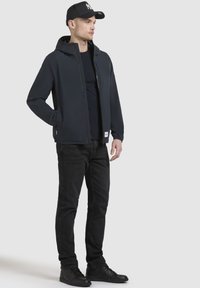 Mørk navy hættejakke med fuld frontlynlås, parret med en sort T-shirt med rund hals og sorte jeans, suppleret med sorte sneakers.