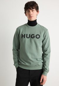 Grønn bomullssweatshirt med rund hals og stor svart "HUGO" tekstlogo foran. Lange ermer med ribbestrikkede mansjetter og kant.