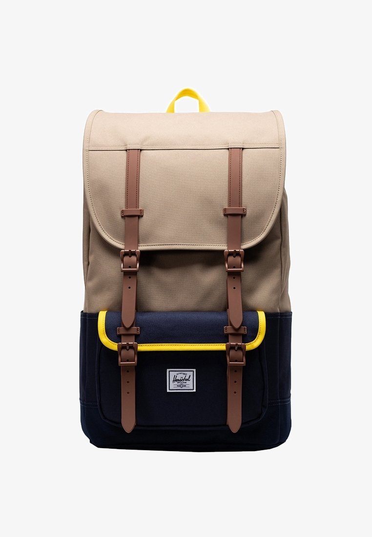 Kangaskauppa ruskeassa ja laivastonsinisessä värissä, jossa on kaksi ruskeaa nahkahihnaa, keltaisia korostuksia etutaskussa ja ylälaidassa suljettava läppä.