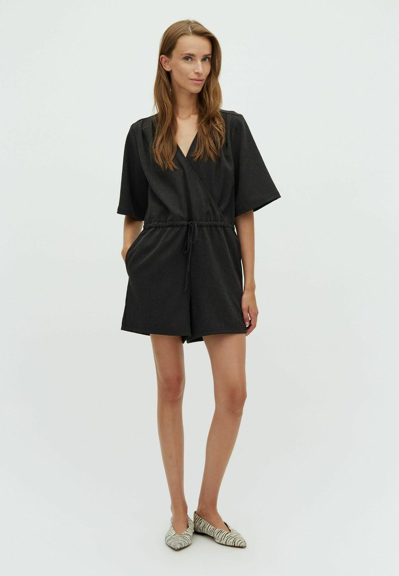 Combinaison courte noire à manches courtes avec taille à cordon. Fabriquée en tissu texturé, elle présente un décolleté en V et des poches latérales.