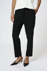 Pantaloni neri su misura con un fit rilassato, caratterizzati da una vita elastica e un dettaglio con zip. Abbinati a décolleté nere con cinturino alla caviglia.