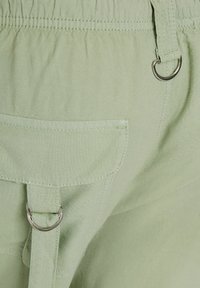 Ljusgröna bomullsshorts med elastisk midja, två metallöglor och en bakficka. Slät textur med ton-i-ton sömnadsdetaljer.