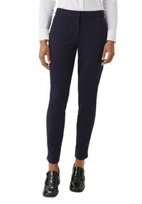 Marineblauwe op maat gemaakte broek met een gladde textuur, slim fit en plooien aan de voorkant, gecombineerd met zwarte gepatineerde loafers en een wit shirt.