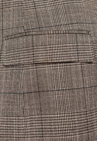 Brązowa materiał w kratę charakteryzuje się połączeniem jasnych i ciemnych nitek, tworząc teksturowany wzór z pionowymi i poziomymi liniami.